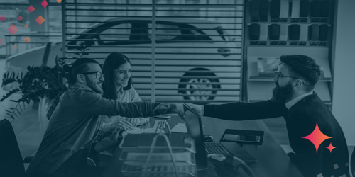 Couple shaking hands with a dealership representative across a desk during the car-buying process.