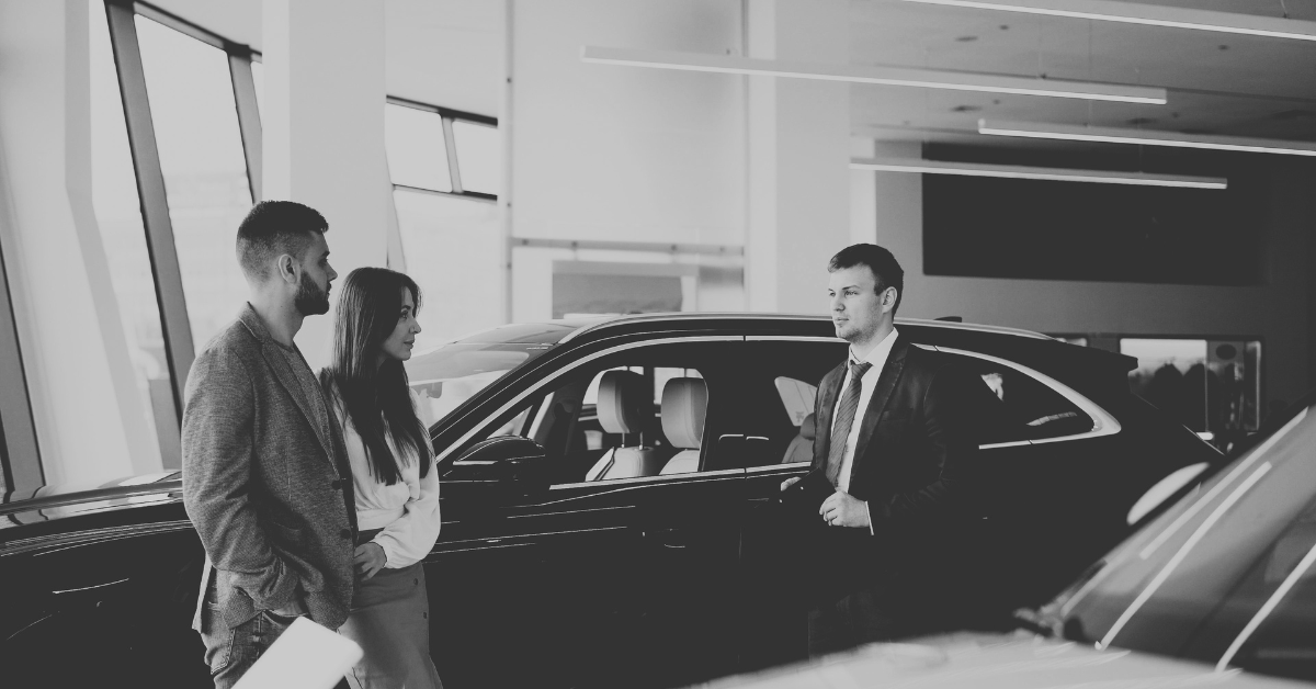 Young couple talking to car salesman in dealership