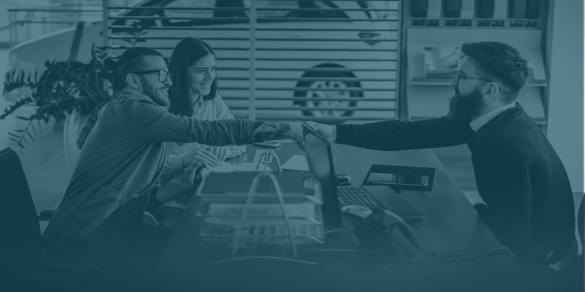 Couple shaking hands with a dealership representative across a desk during the car-buying process.